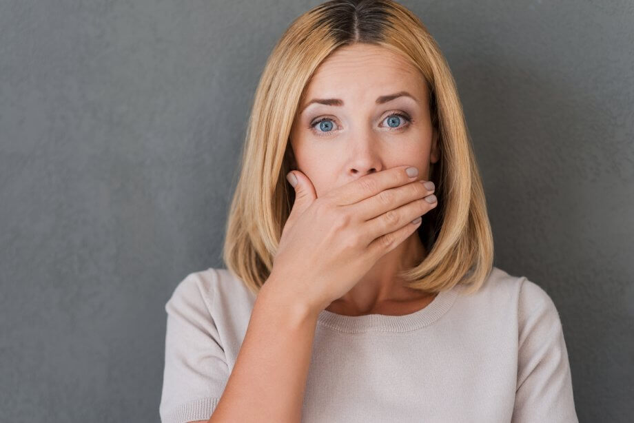 Photograph of a Woman with Short, Straight Blonde Hair Holding Her Right Hand Over Her Mouth