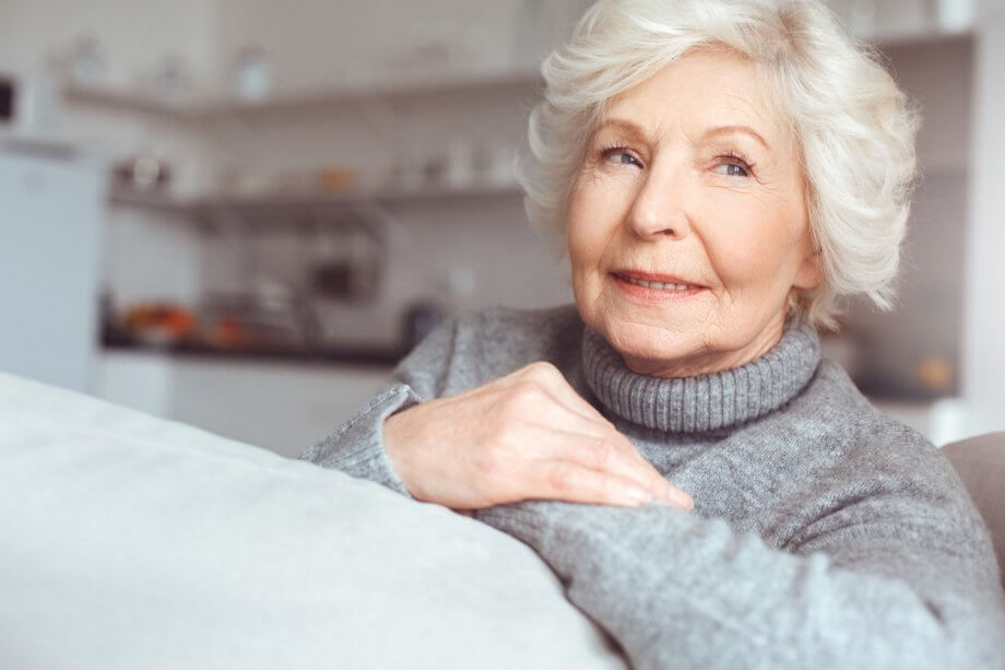 An Older Woman with Short, Wavy White Hair Sitting in a Home Setting Looking Off Into Distance