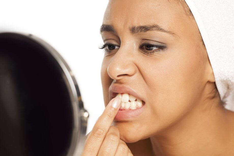 Young Woman Looking at her Teeth in the Mirror Unhappily While Rubbing Them with Finger