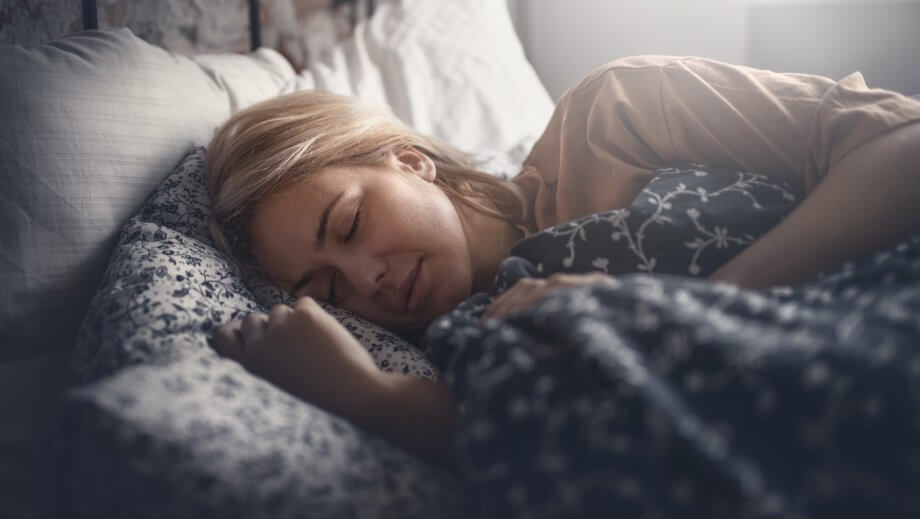 Woman with Blonde Hair Sleeping Under Blankets in Bed