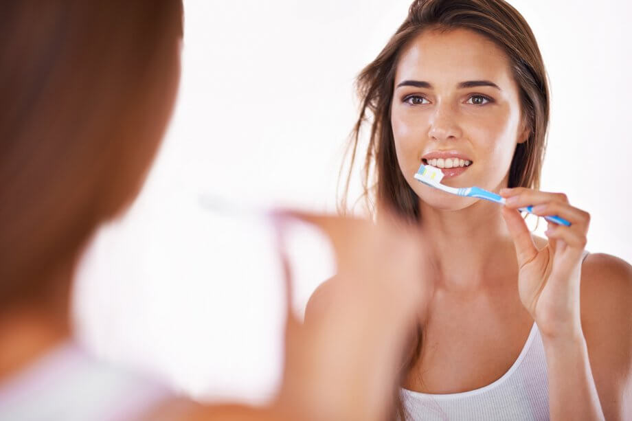 woman brushing teeth in mirror